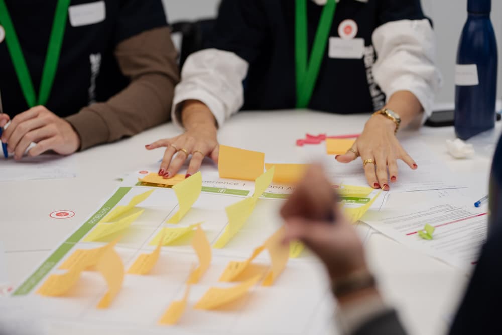 Participantes a colaborar numa mesa de trabalho com notas adesivas e materiais de workshop